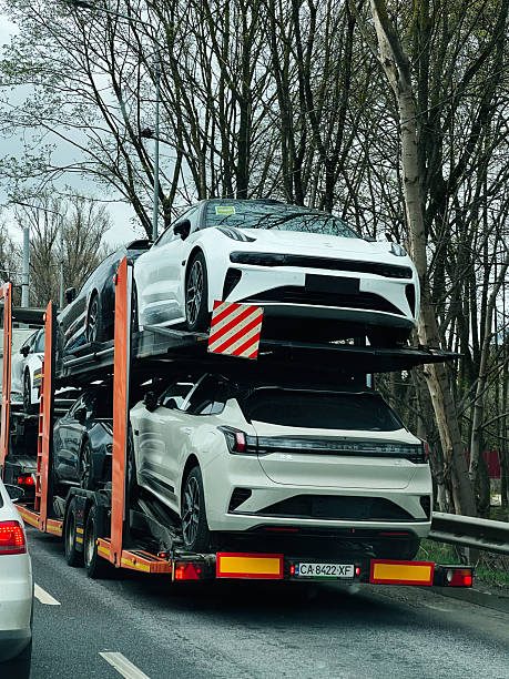 A transporter lorry carrying a vehicle on a tree-lined road