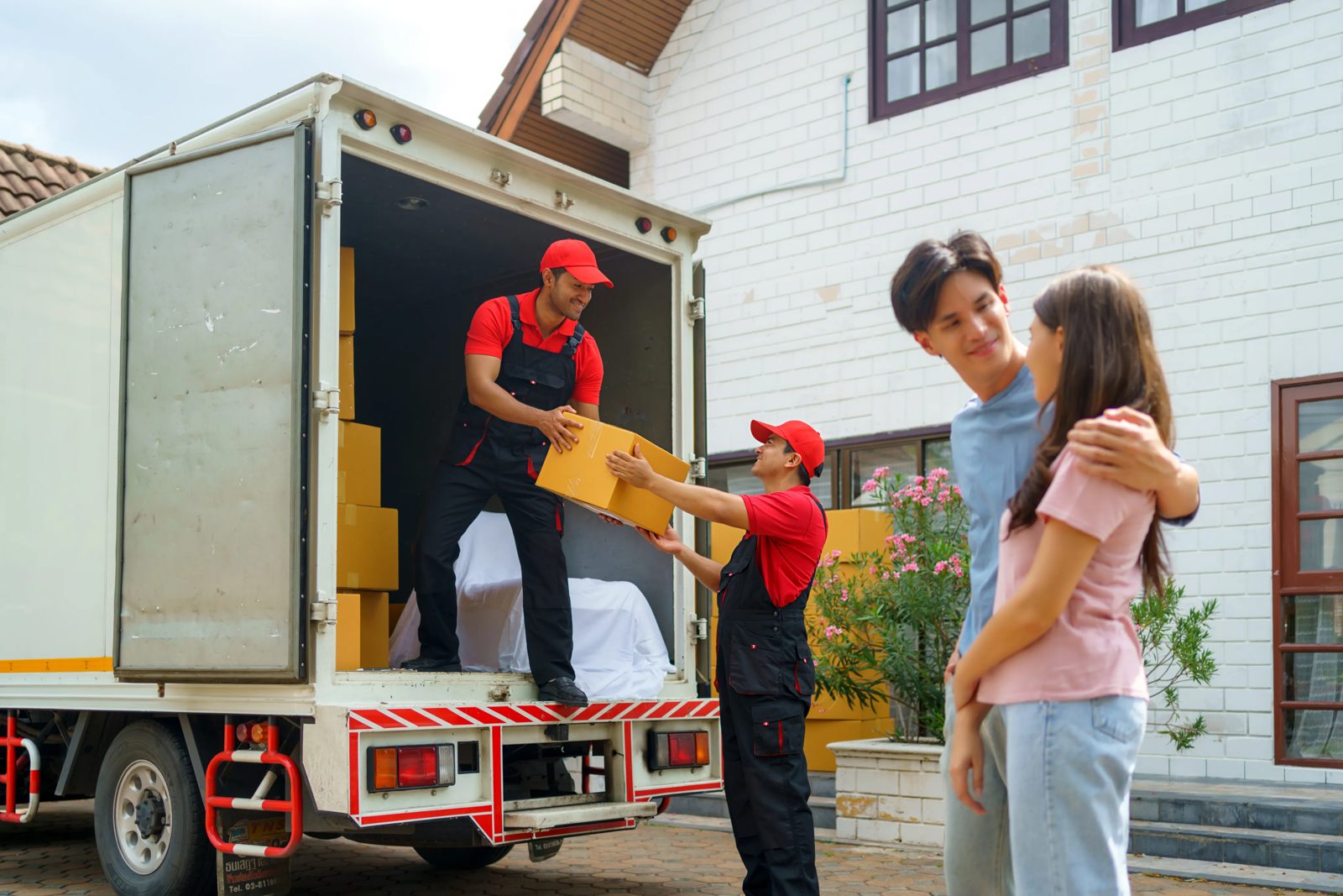 Two movers unloading boxes from a removal van outside a family home